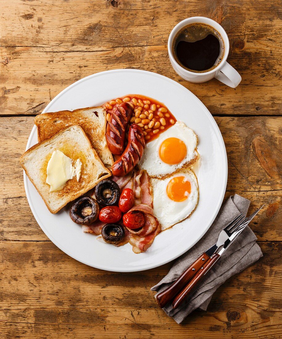 Englisches Frühstück mit Spiegeleiern, Würstchen, Speck, Bohnen, Toast, Tomaten und Pilzen