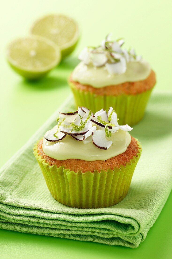 Fresh coconut and lime iced cupcakes on a green napkin and green background with 2 half limes