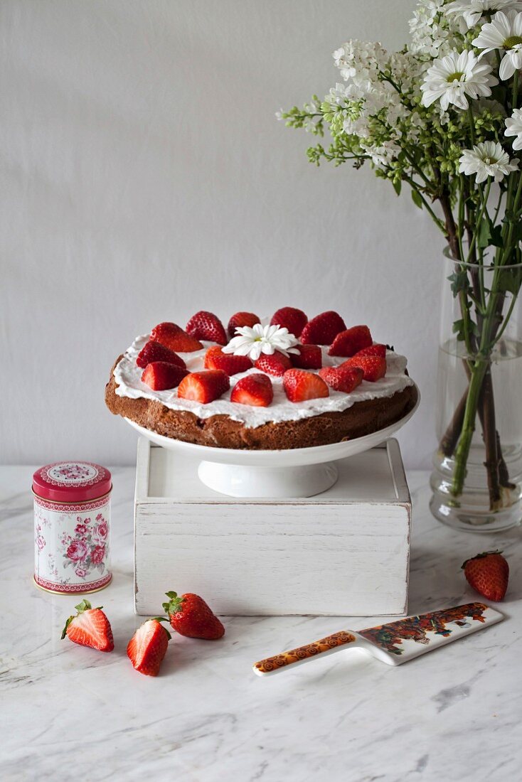 Strawberry cake with whipped coconut cream and topped with fresh strawberries on a white cake stand