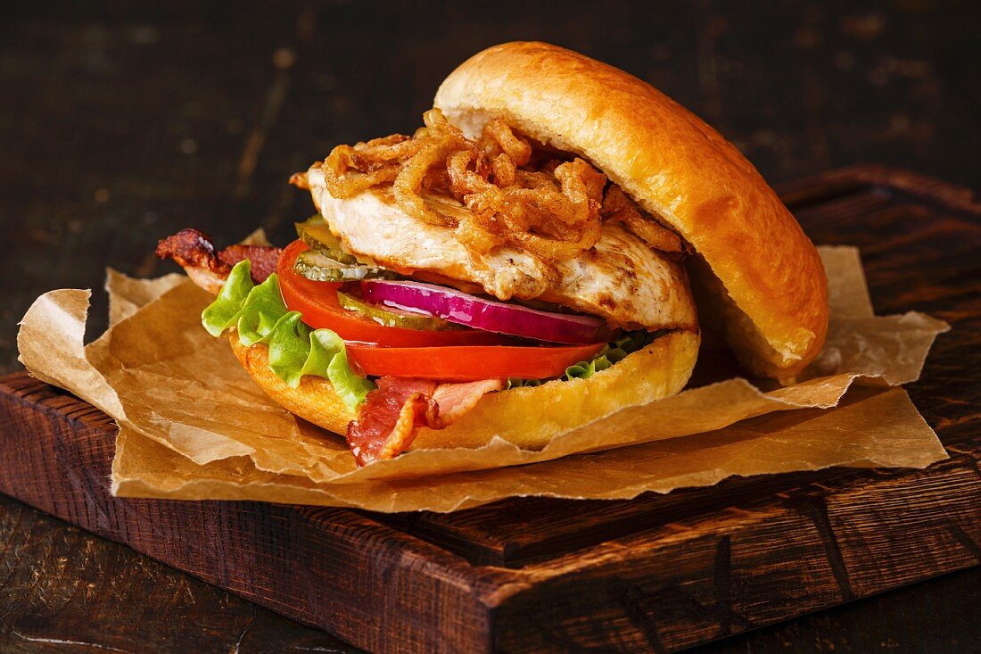 Burger with chicken breast and fried onions on dark background