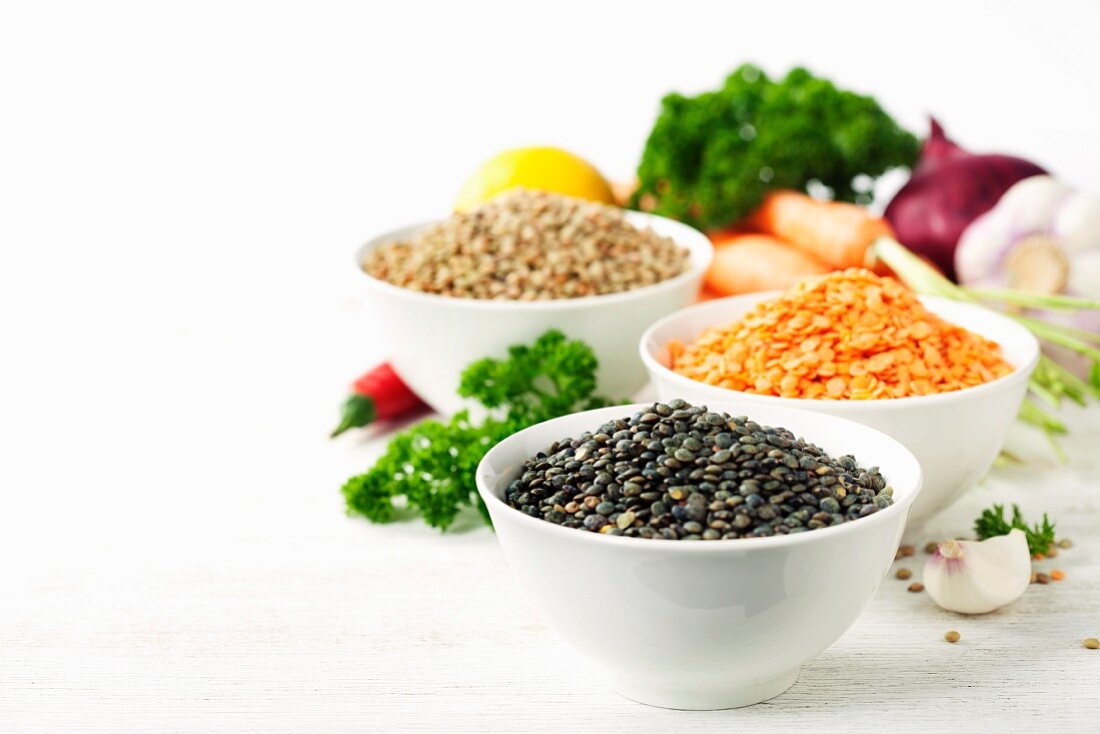 Bowls of assorted dried lentils with vegetables over white