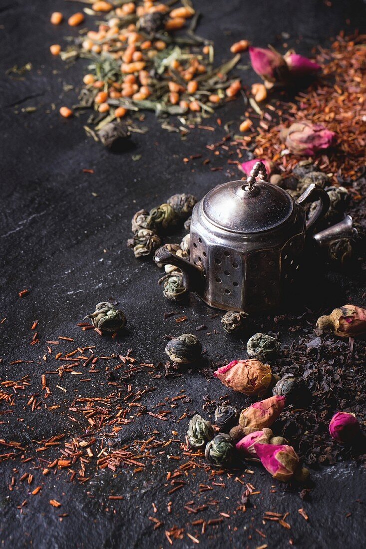 Assortment of dry tea with tea strainer: Green tea, black tea, green tea with rice, rooibos, dry rose buds