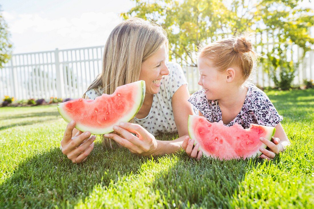 Mutter und Tochter essen Wassermelone auf der Wiese liegend