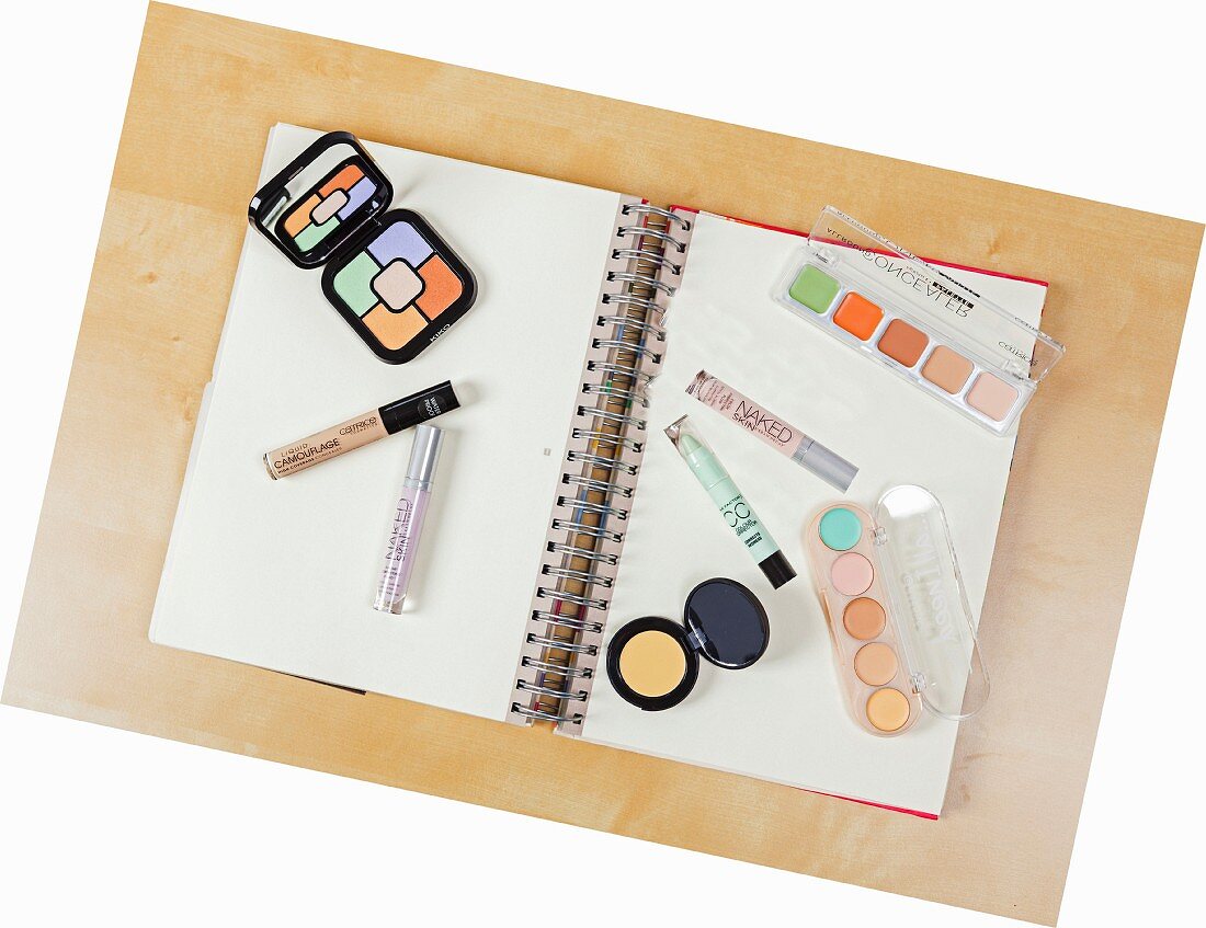 Various cosmetic products for colour-correcting laid out on a spiral-bound notebook