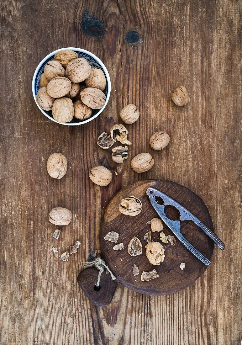 Walnuts in ceramic bowl and on wooden board with nutcracker over rustic wooden background