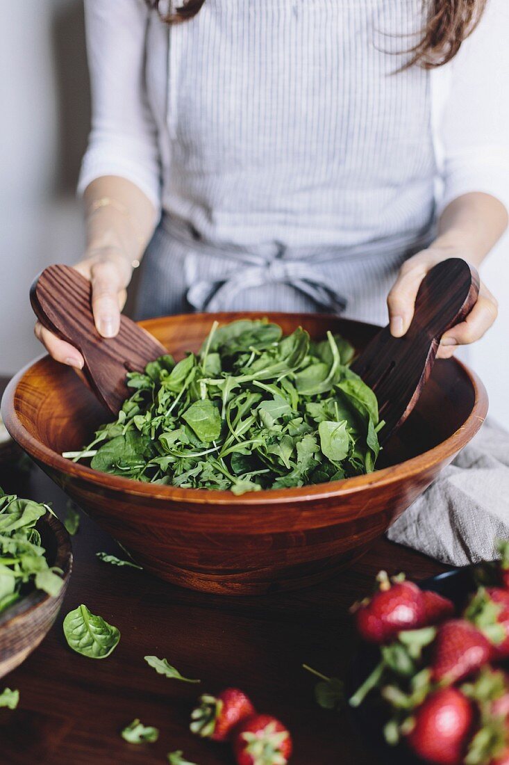 A woman is mixing spinach and arugula to make a strawberry spinach and arugula salad