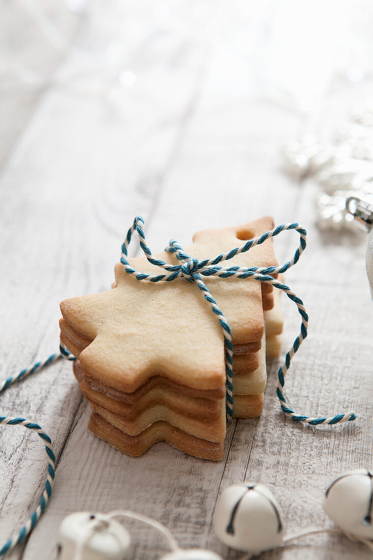A Stack of tree shaped biscuits tied with blue and white bakers twine in a white Christmas setting