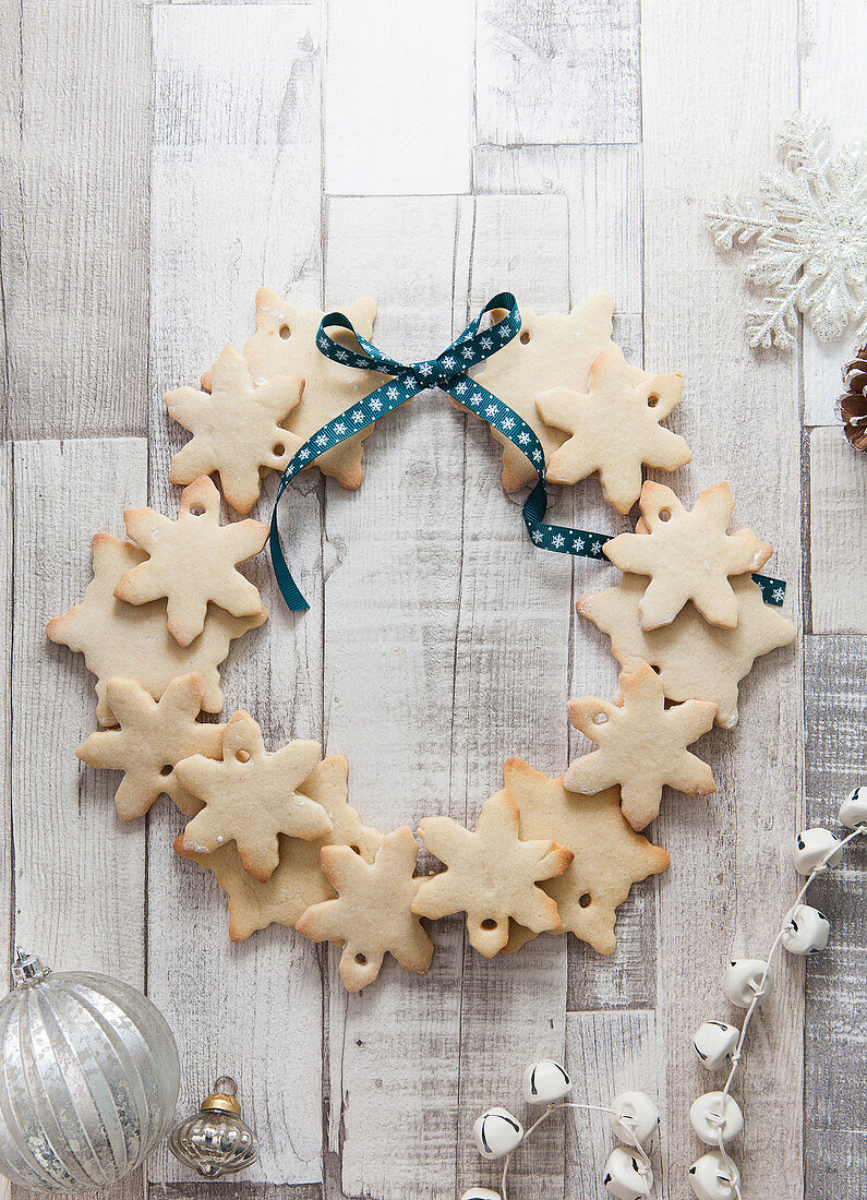 Snowflake shaped biscuits arranged to make a Christmas wreath on a rustic white wood surface