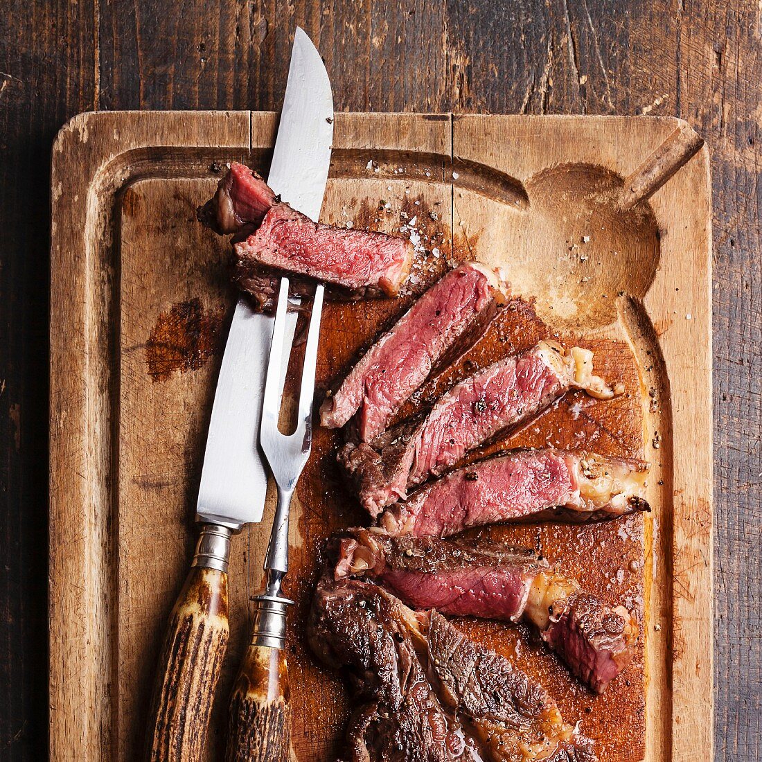 Medium rare Beef steak Ribeye with knife and fork for meat on cutting board on dark wooden background