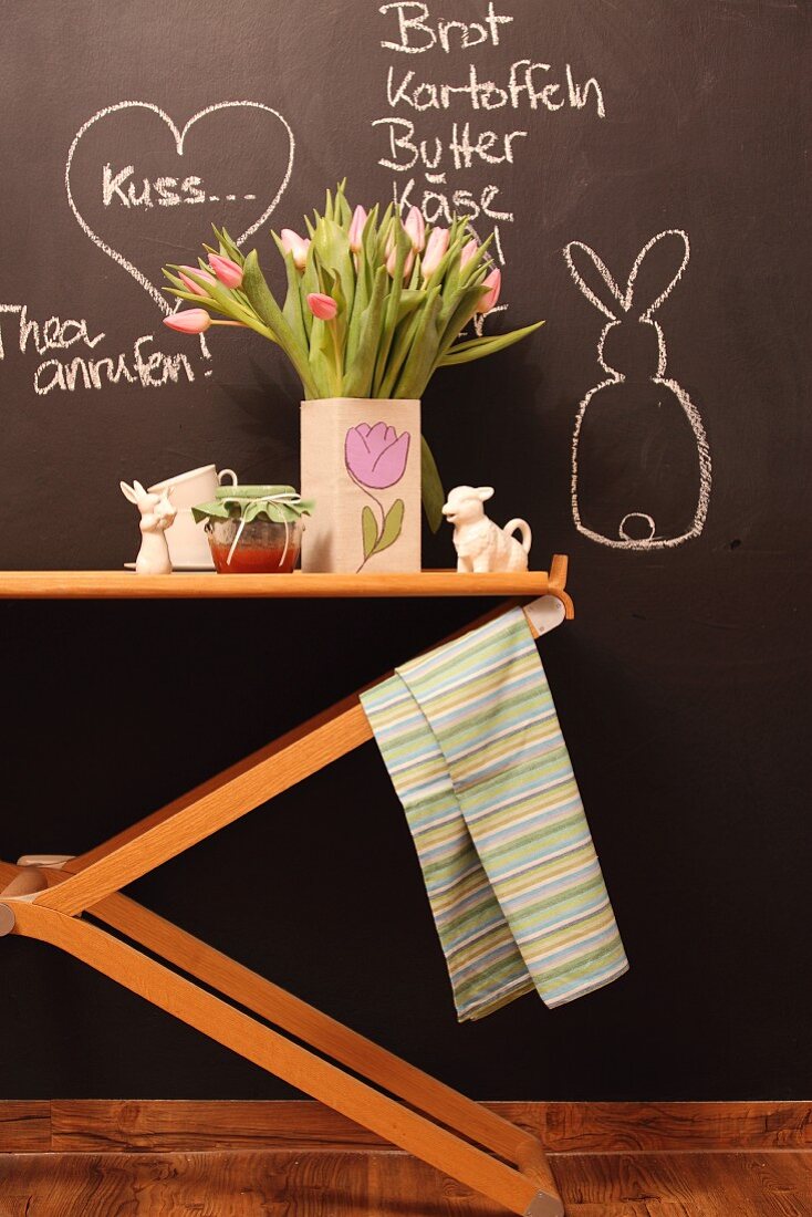 Vase of tulips and Easter ornaments on wooden table against chalkboard wall with chalk messages