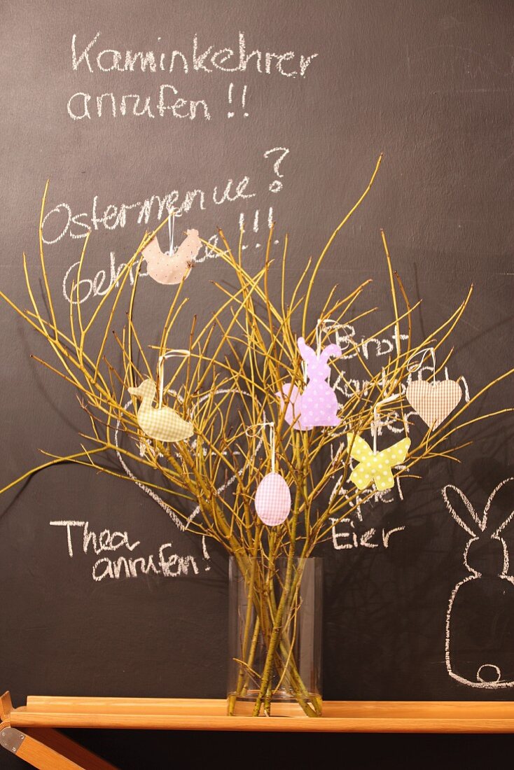 Easter arrangement in glass vase on wooden table against chalkboard with chalk messages
