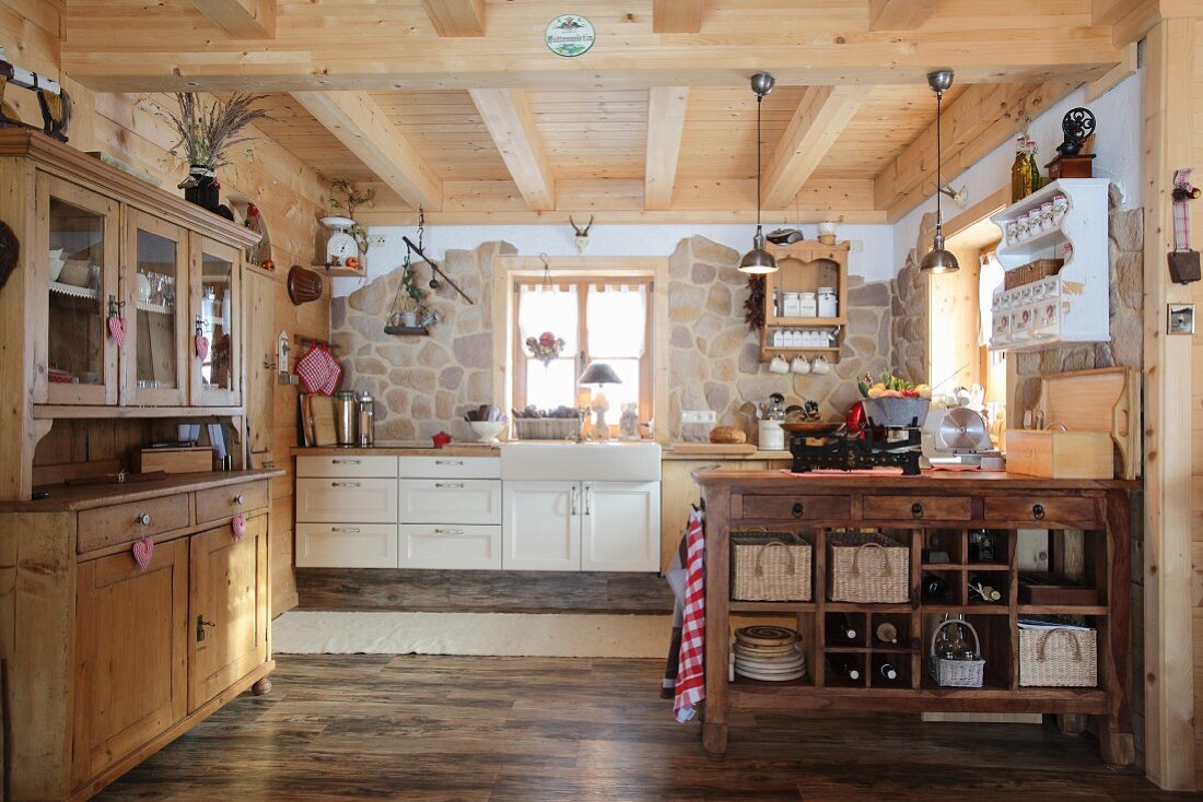 Dresser, island counter and one stone wall in open-kitchen of wooden cabin