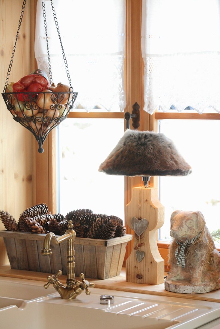 Rustic ornaments and table lamp on windowsill behind sink with vintage taps