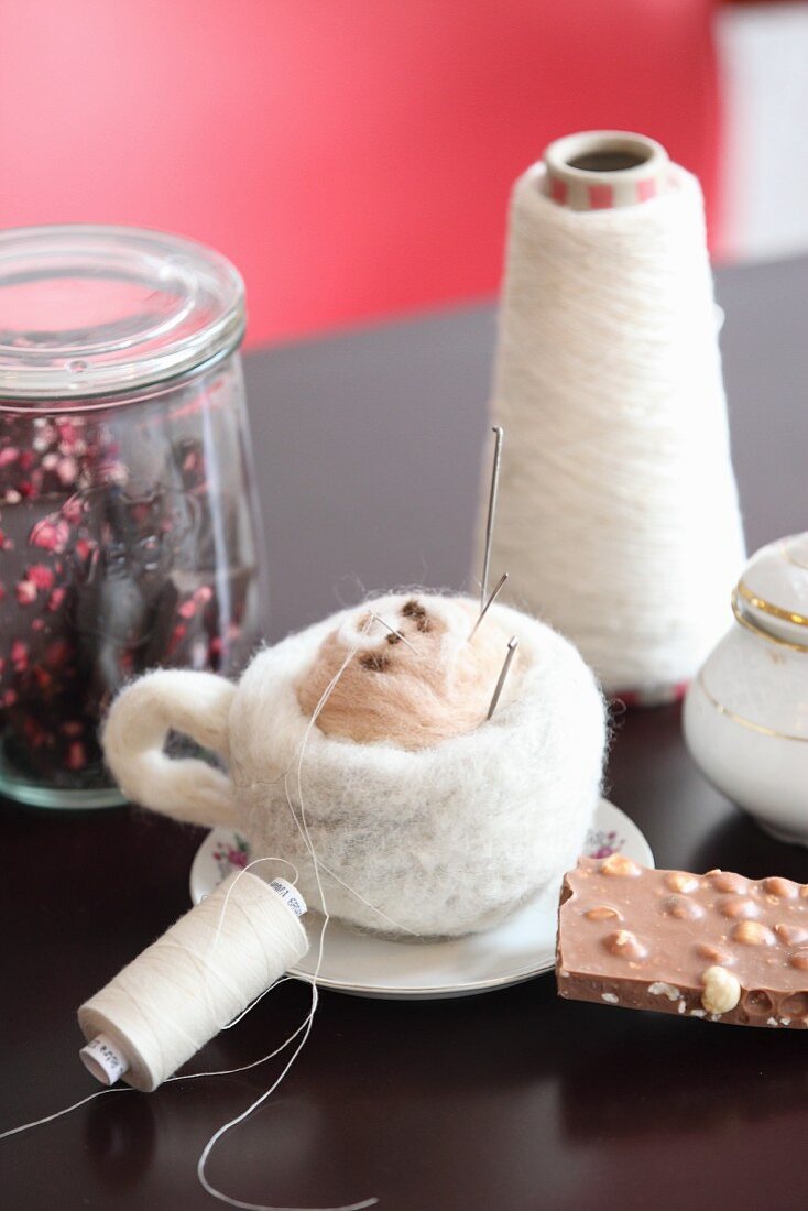 Needle-felted a cup of cappuccino, chocolate, sugar bowl, Gerbera daisy, yarn and glass jars on table