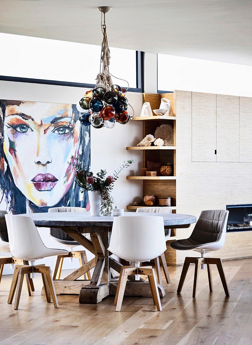 Round table with chairs in front of large-format portrait painting in a bright dining area