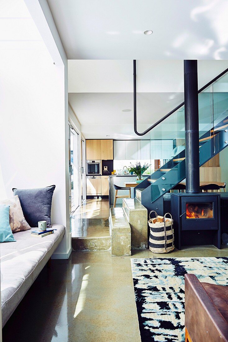 Open living area with polished concrete floor, built-in bench in front of the window and fireplace, in the background stairs with glass balustrade