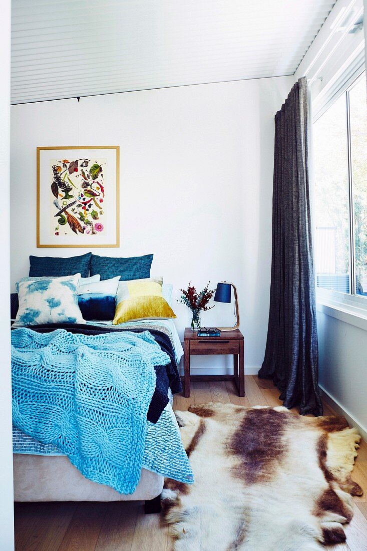 Blue knitted bedspread on double bed and animal fur rug in bedroom