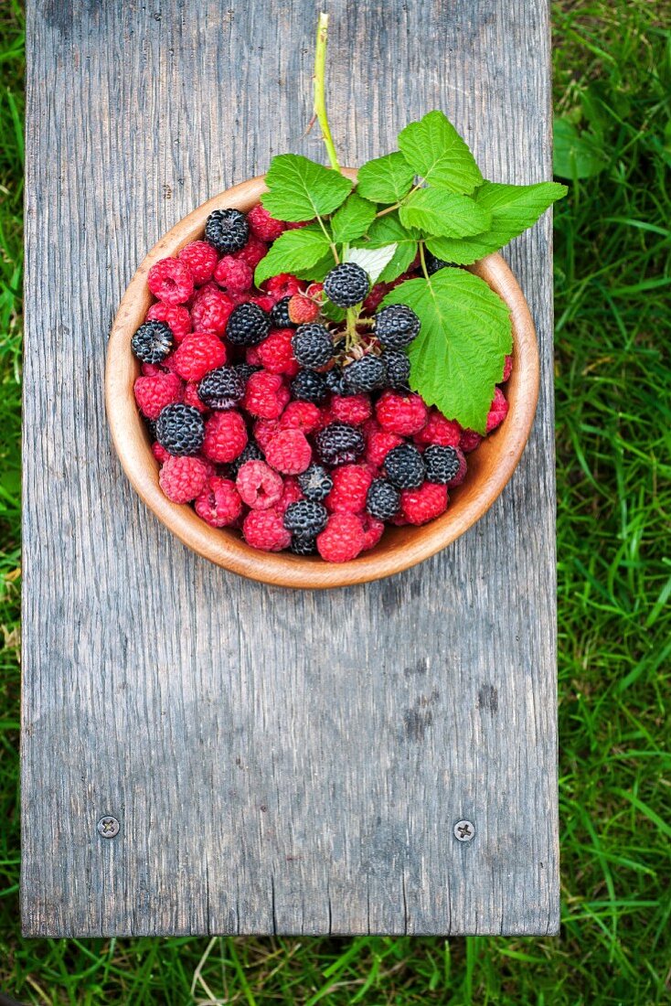 Fresh raspberries and blackberries in a bowl on a wooden board