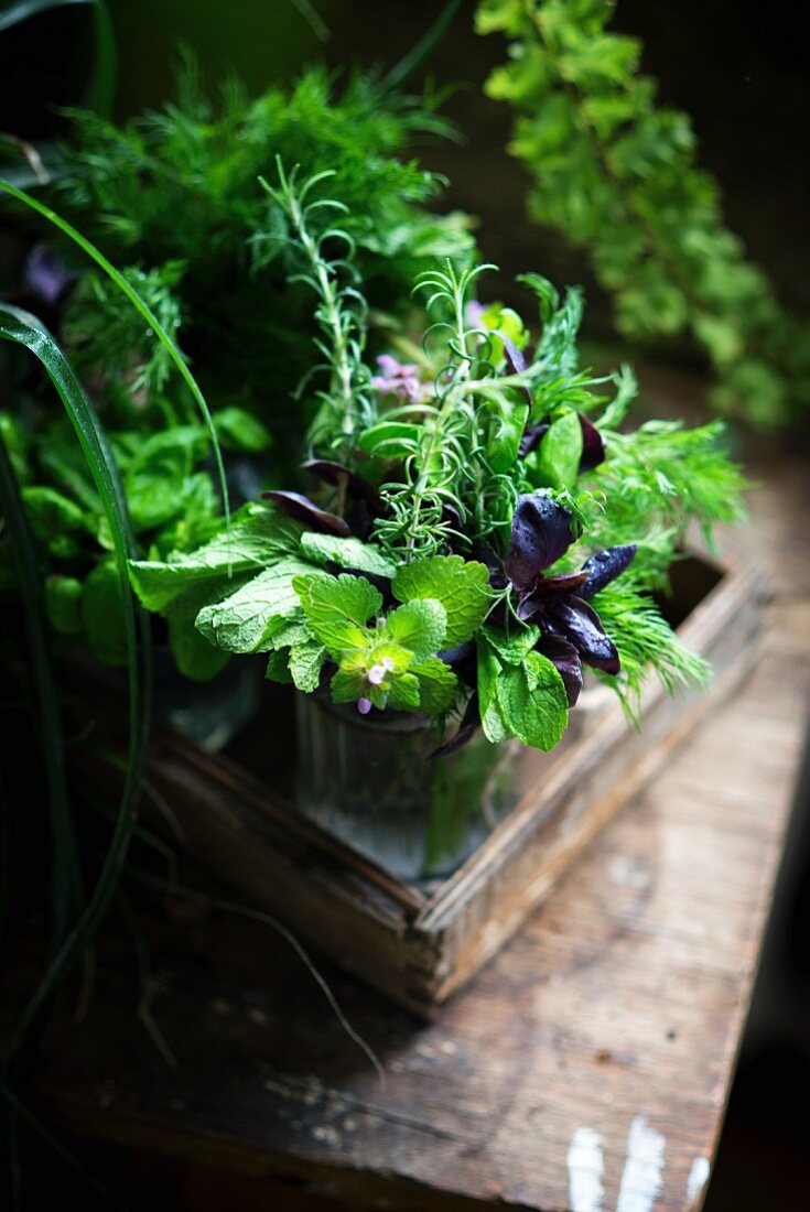 Fresh herbs in a water glass on a wooden tray