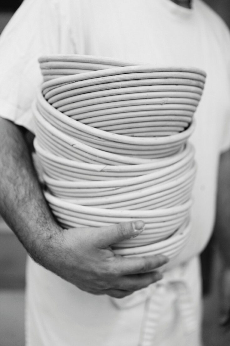 A baker holding a pile of fermentation baskets