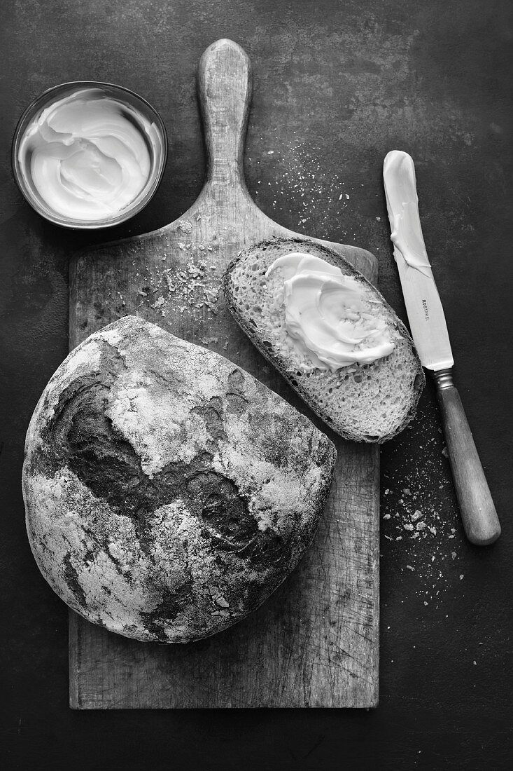 Angeschnittener Brotlaib und Brotscheibe mit Butter auf Holzbrett