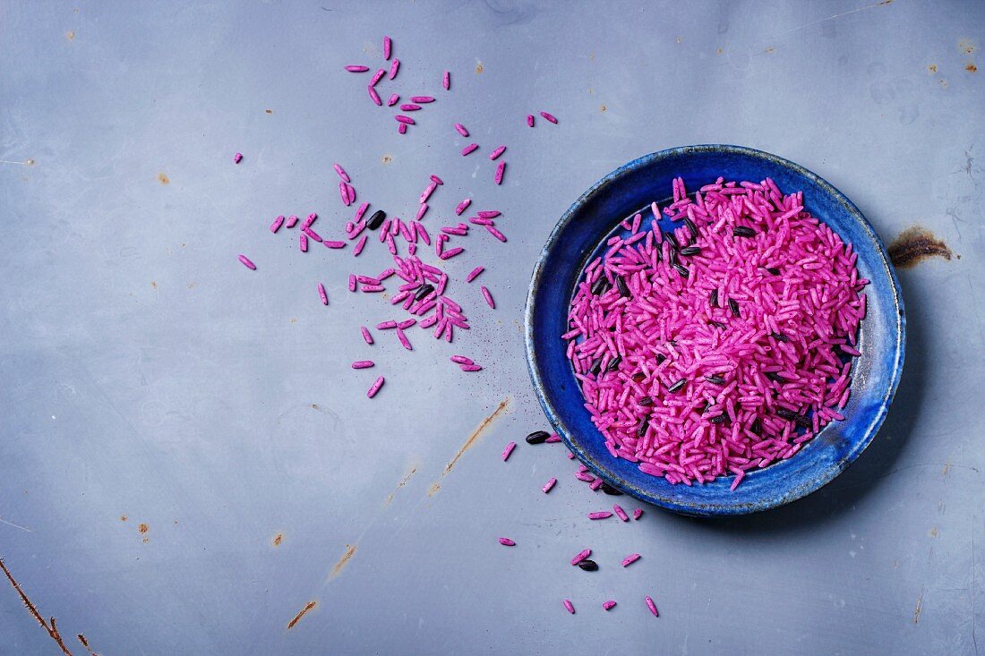 Uncooked pink rice on blue ceramic plate over gray metal surface