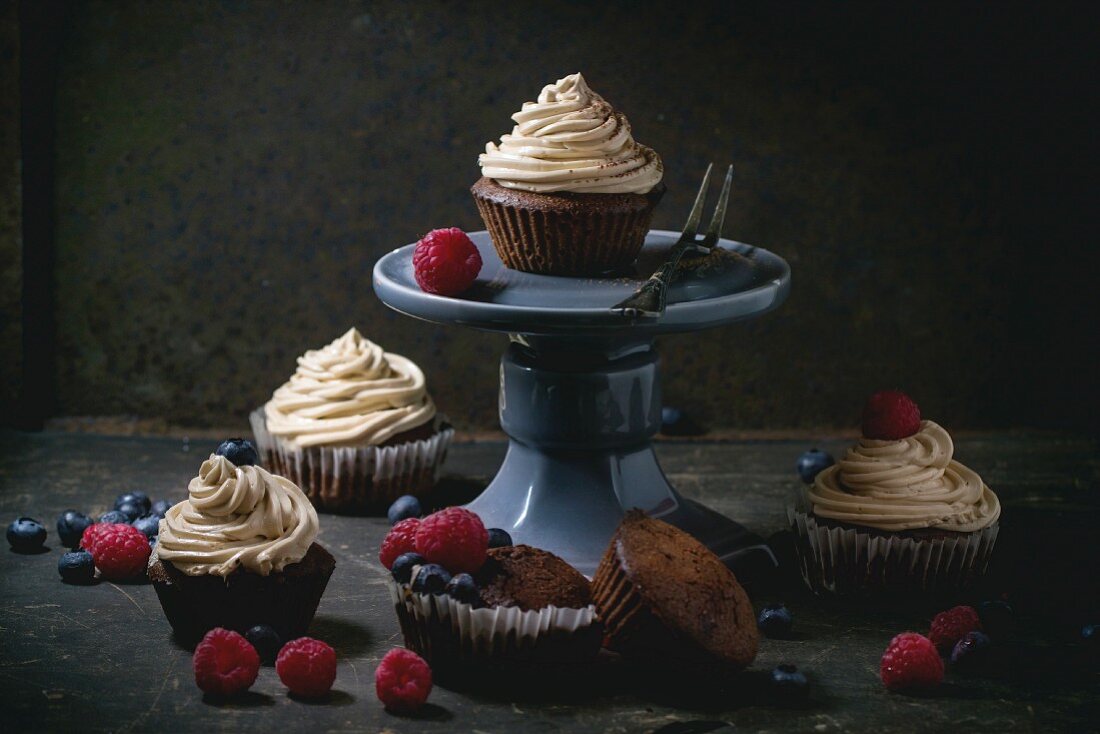 Chocolate cupcakes with butter coffee cream and fresh berries over dark background