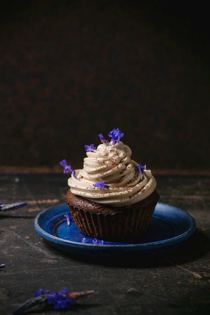 Chocolate muffin with coffee butter cream and edible lavender flowers over dark surface