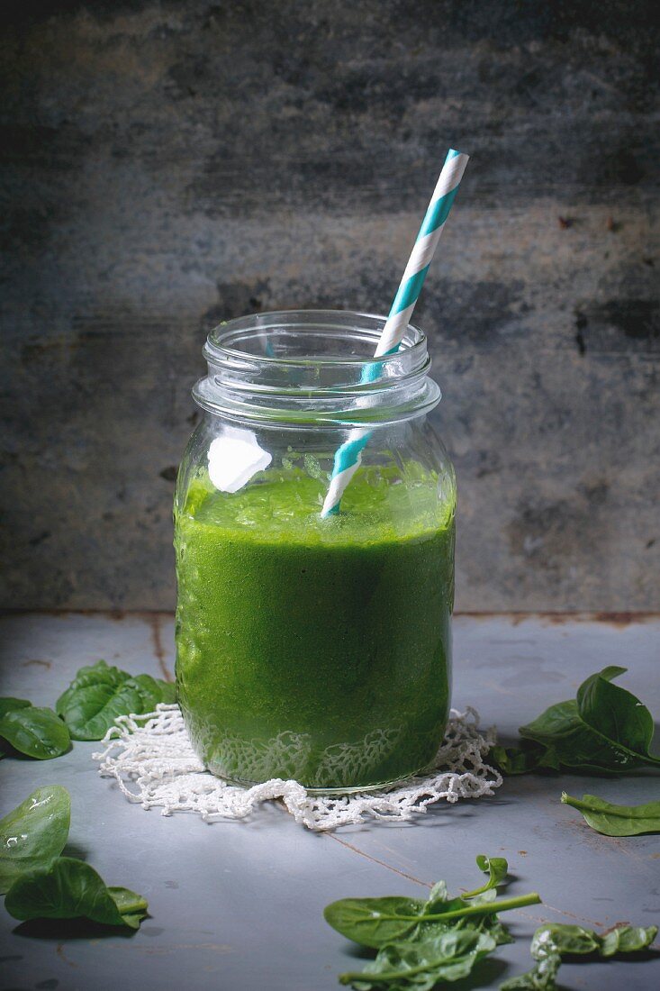 Glass jar with green smoothie, served with baby spinach leaves over metal table