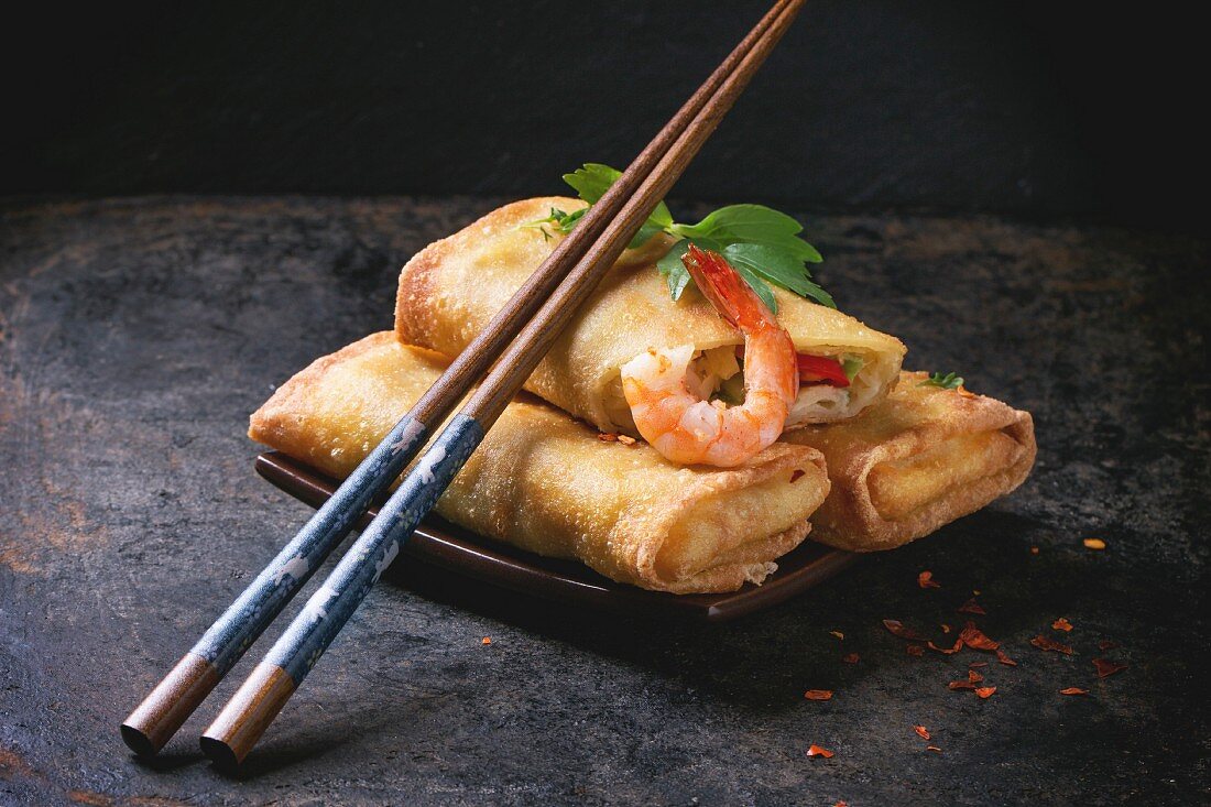 Fried spring rolls with vegetables and shrimps, served on squer ceramic plate with chopsticks
