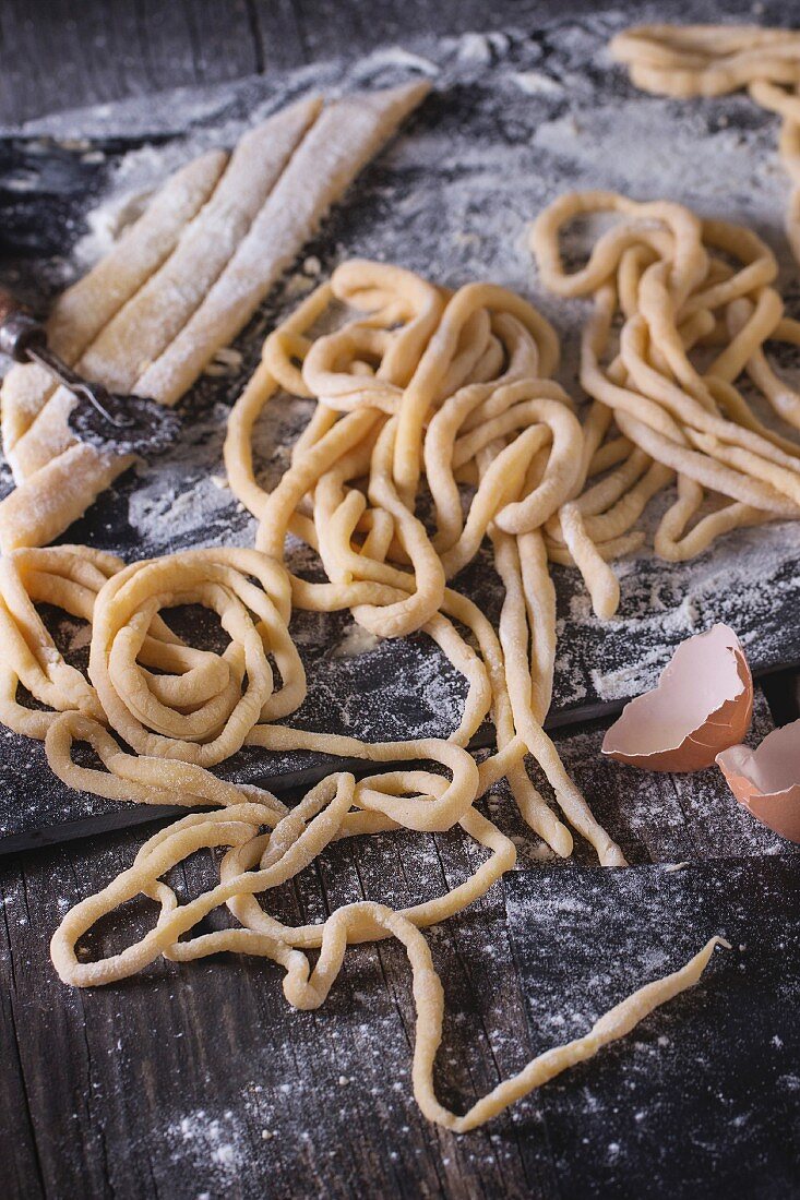 Making homemade pasta pici: sliced rolled dough for pasta and prepared long pasta on black slate board