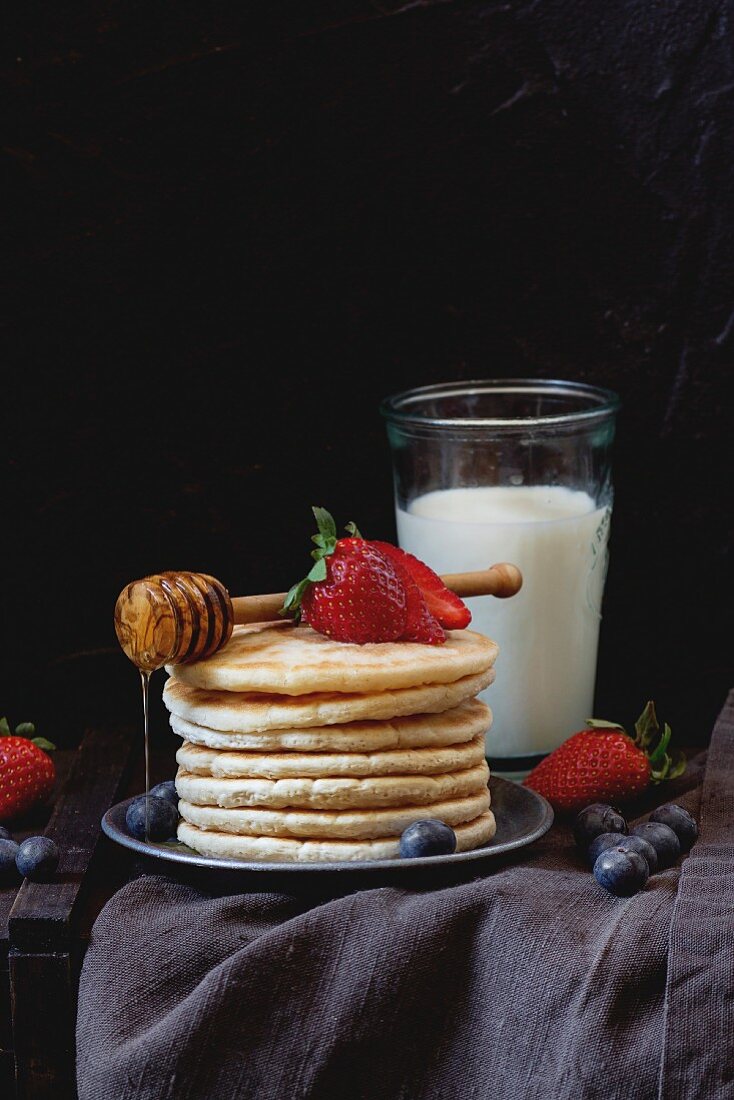 Ein Stapel Pancakes mit Honig und Beeren, dazu ein Glas Milch