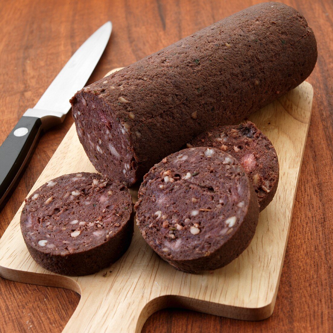 Uncooked English black pudding on cutting board with knife