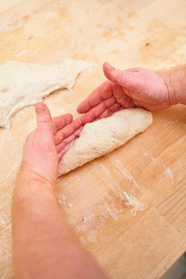 A piece of dough being separated with the wet edges of a man's hands