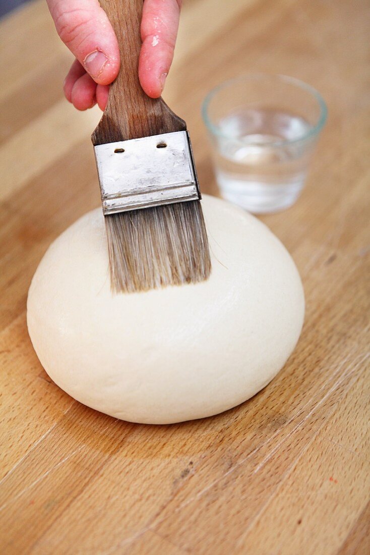 A piece of dough being moistened with a brush