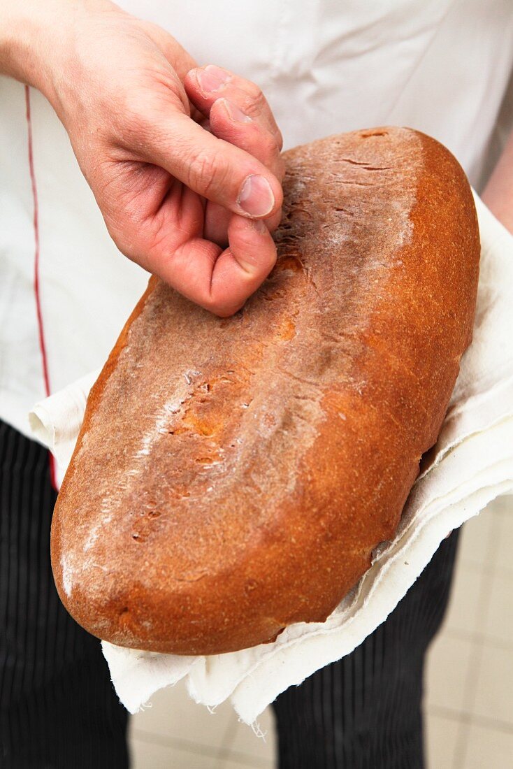 A baker tapping the bottom of a loaf of bread