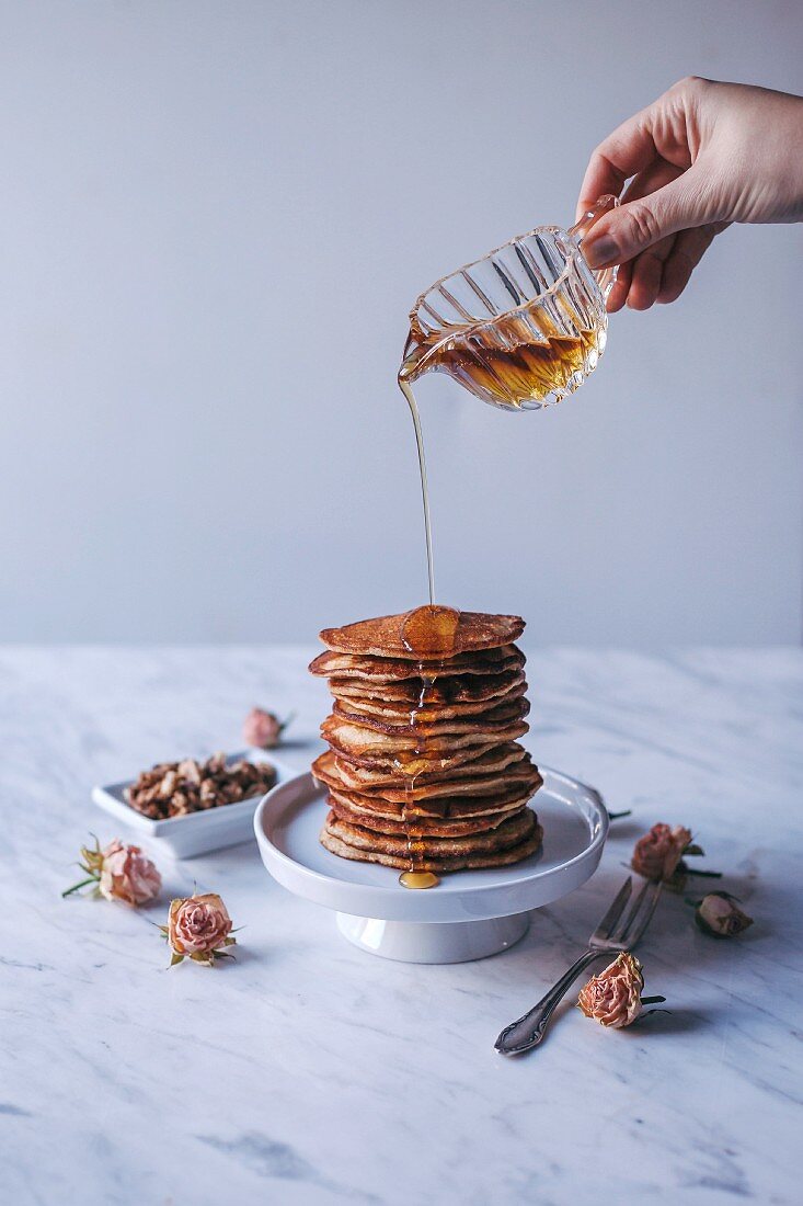 Woman puring maple syrup over stack of pancakes