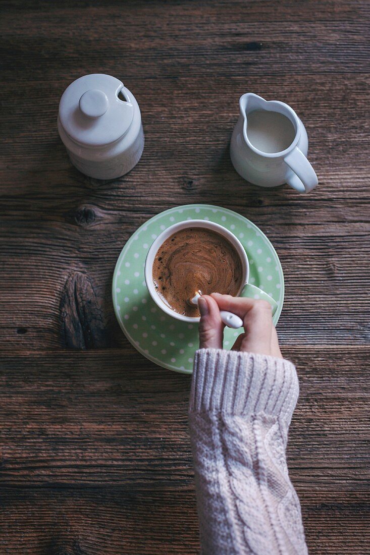 A womans hands stiring a cup of strong black coffee, with milk and sugar.
