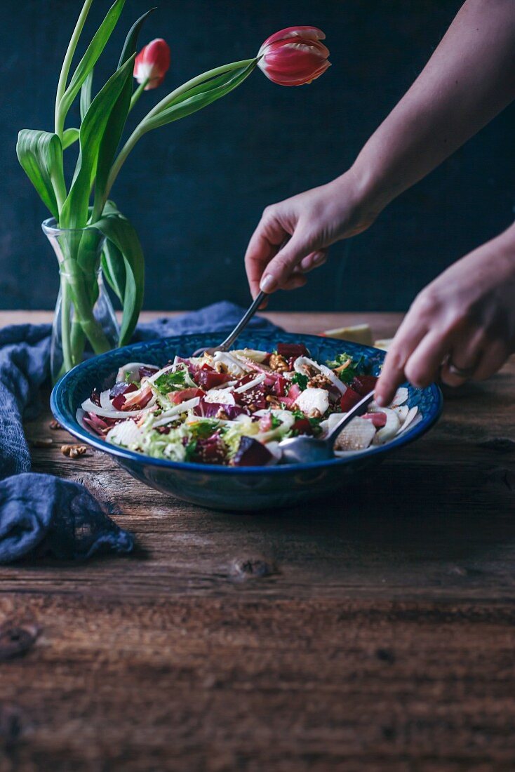 Frau vermischt Salat mit Rote-Bete, Fenchel und Apfel in Salatschüssel