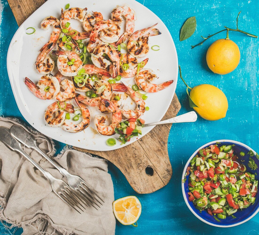 Grilled tiger prawns in white plate with lemon, leek, chili pepper and mint salsa sauce on wooden board