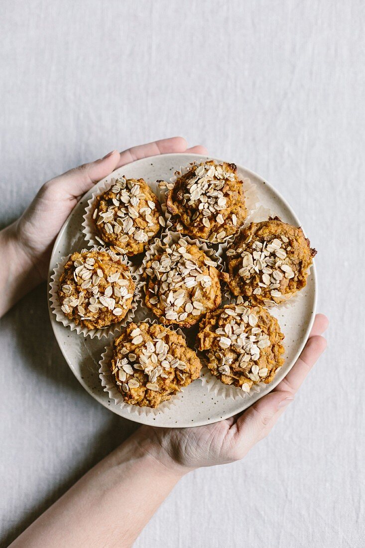 A woman is holding a plate full of freshly baked sweet potato muffins