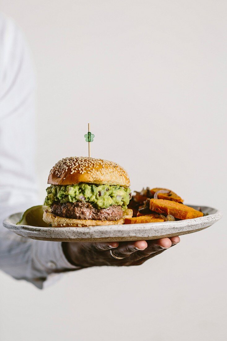 A man is holding a plate of guacamole burger and sweet potato fries