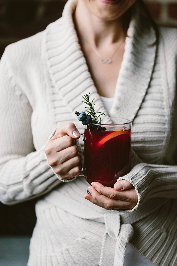 A woman with a glass of blueberry hot toddy in her hand