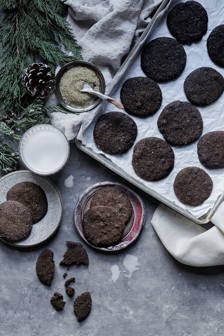 Weihnachtsplätzchen auf Backblech und Teller, dazu ein Glas Milch (Aufsicht)