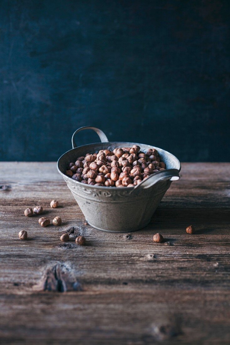 Raw hazelnuts in a metal bucket on a wooden table