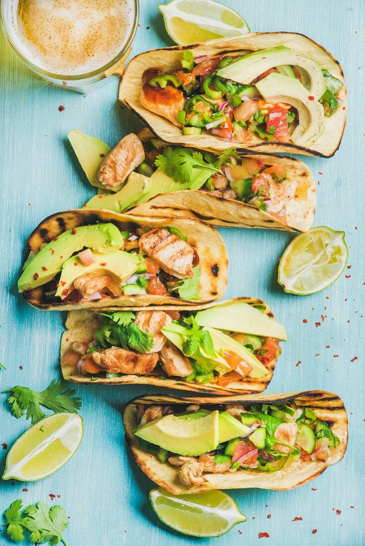 Healthy corn tortillas with grilled chicken, avocado, fresh salsa, limes and beer in glass