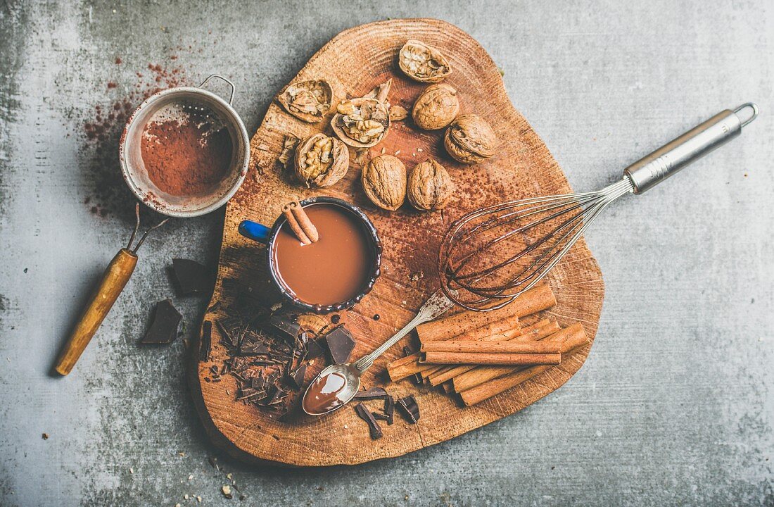 Rich winter hot chocolate with cinnamon sticks and walnuts in blue enamel mug on wooden board