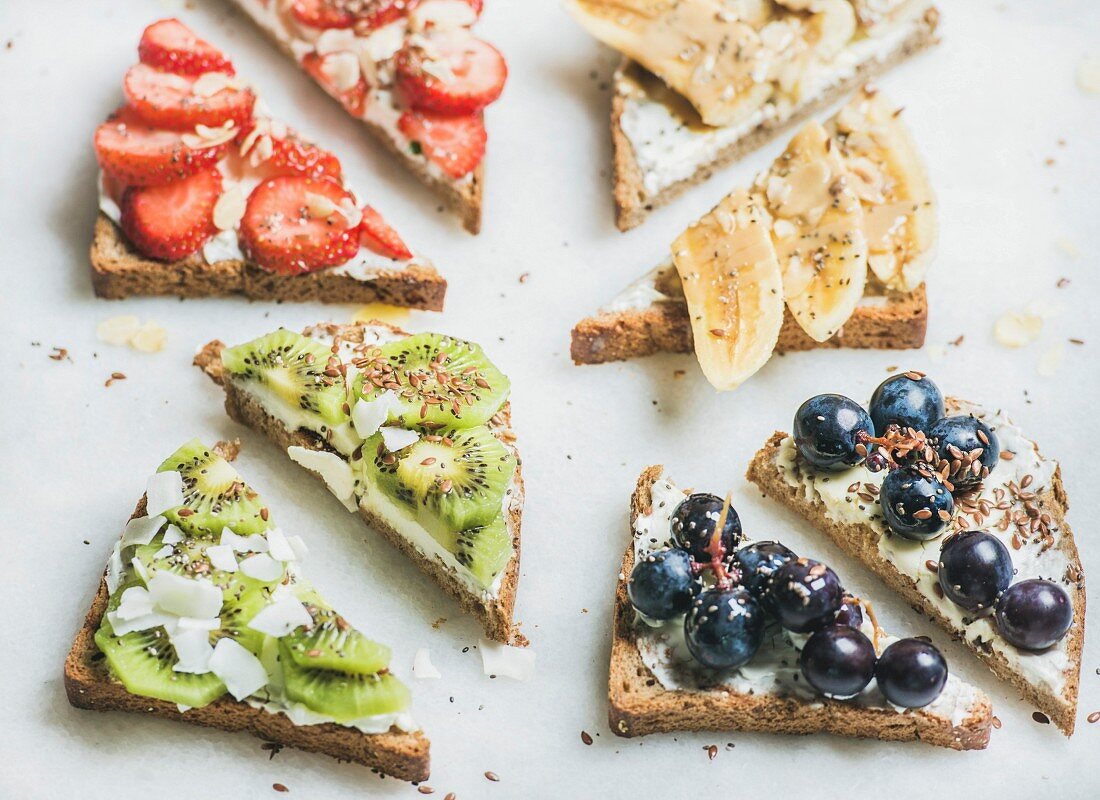 Healthy breakfast wholegrain bread toasts with cream cheese, various fruit, seeds and nuts, top view