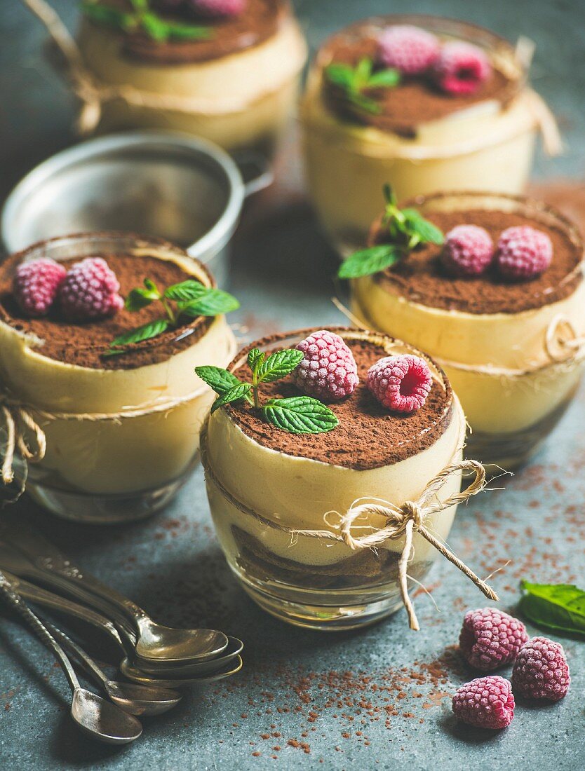 Tiramisu served in individual glasses with frozen raspberries, fresh mint leaves and cocoa powder