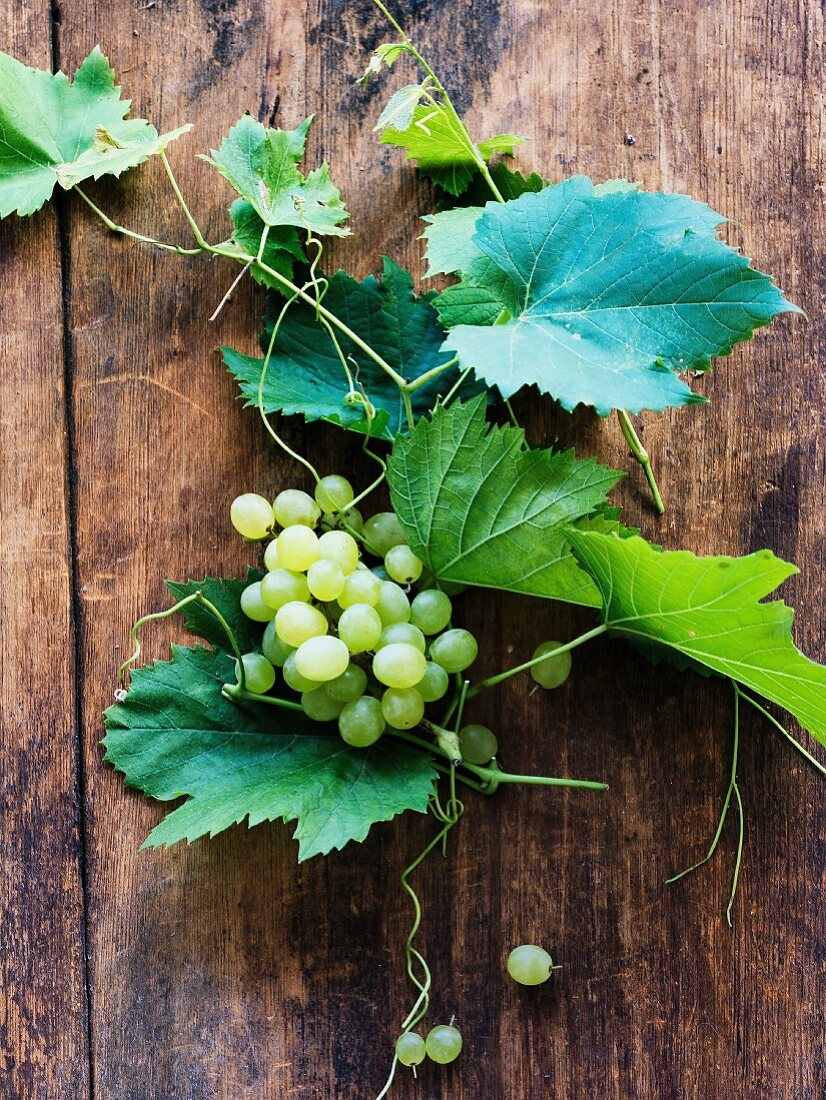 Grüne Trauben mit Weinblättern auf Holzuntergrund
